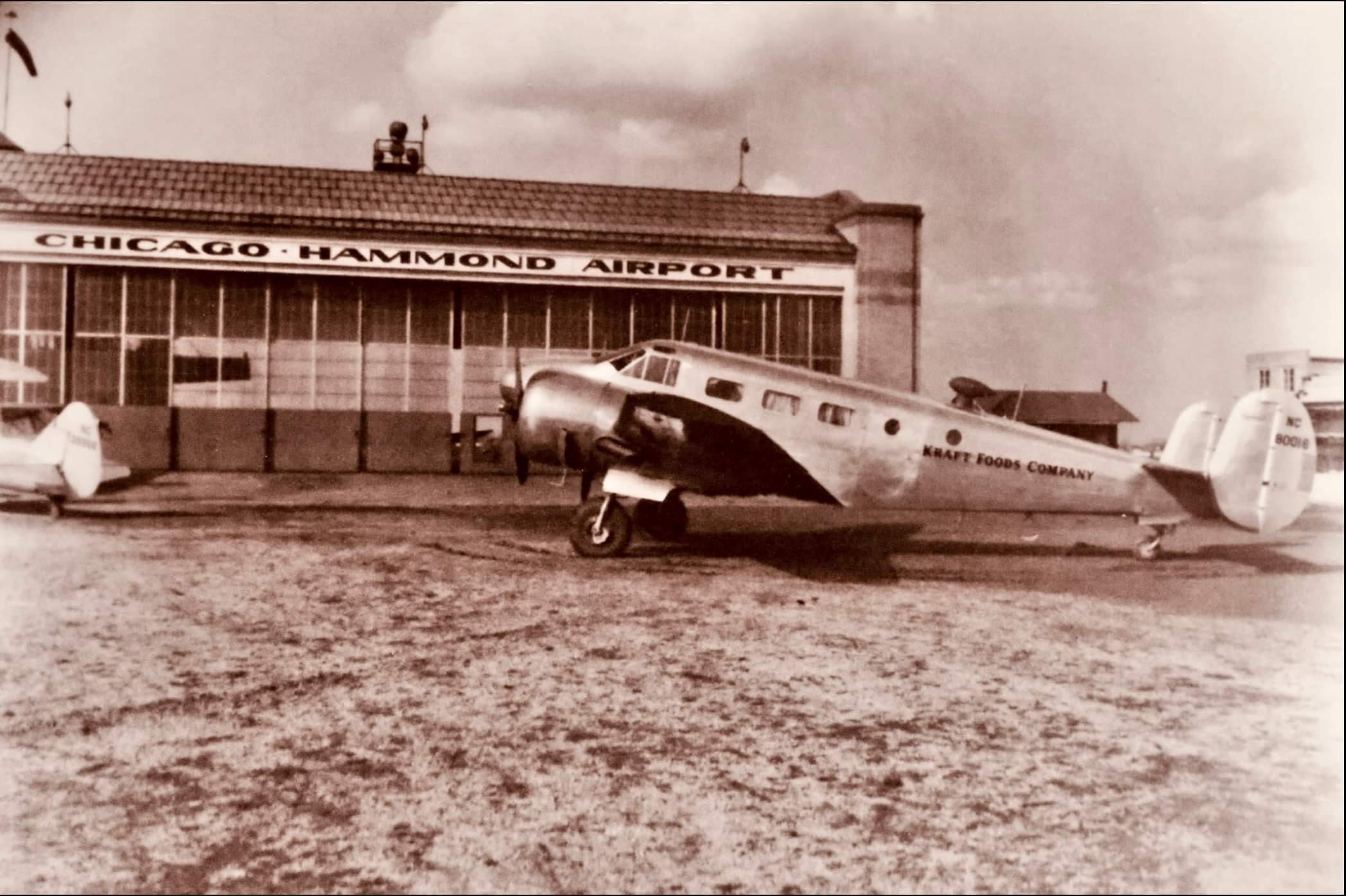 an old photo of a plane in front of the now ford airport hangar in sepia tones